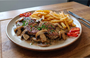 Pork Shoulder with Mushrooms: Juicy Meat with Creamy Sauce and Homemade Fries Pork shoulder with mushrooms, creamy sauce and homemade fries on a plate