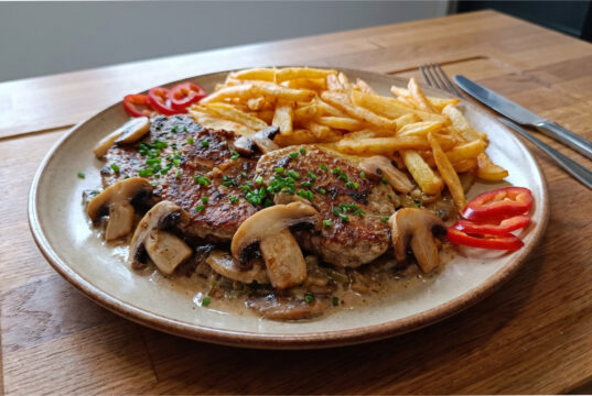Pork Shoulder with Mushrooms: Juicy Meat with Creamy Sauce and Homemade Fries Pork shoulder with mushrooms, creamy sauce and homemade fries on a plate