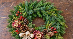 Don’t Buy Expensive All Souls’ Day Wreaths: You Can Easily Make These Beautiful Ideas from Pine Branches and Cones at Home All Souls' Day wreath decorated with pine branches, cones, flowers, red berries and a light bow