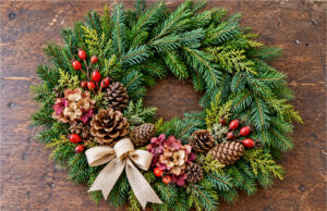 Don’t Buy Expensive All Souls’ Day Wreaths: You Can Easily Make These Beautiful Ideas from Pine Branches and Cones at Home All Souls' Day wreath decorated with pine branches, cones, flowers, red berries and a light bow