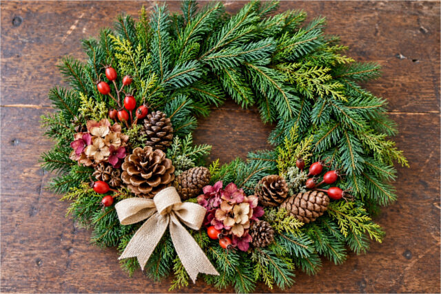 All Souls' Day wreath decorated with pine branches, cones, flowers, red berries and a light bow