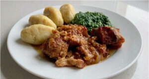 Pork Roast with Potato Dumplings and Spinach: Slow-Roasted Lunch with Beer Gravy Golden roasted pork belly with potato dumplings and creamy spinach on a plate