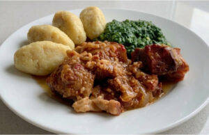 Pork Roast with Potato Dumplings and Spinach: Slow-Roasted Lunch with Beer Gravy Golden roasted pork belly with potato dumplings and creamy spinach on a plate
